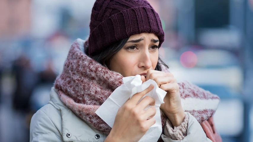 Young woman coughing during winter on street. Girl with cold wearing knitted cap and scarf feeling unwell. Woman feeling sick during for winter and city pollution. Girl with sore throat.